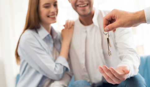 REALTOR® handing a young couple a set of keys to their new home