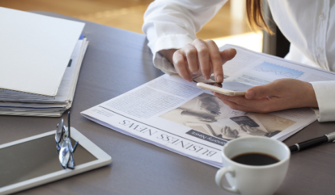 Woman using her phone and reading a newspaper on the table with coffee